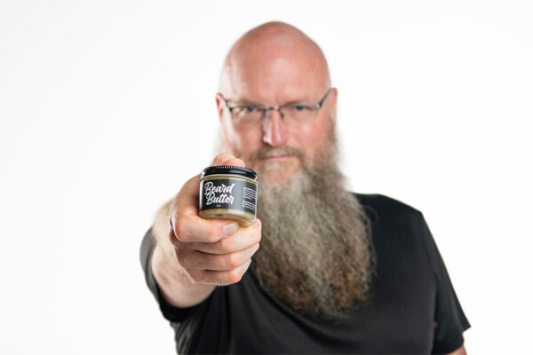 Bearded man holding jar of Beard Butter beard care in close up view to the viewer.