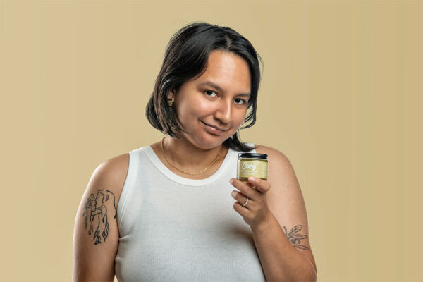 Woman in white tank top holding jar of skin salve.