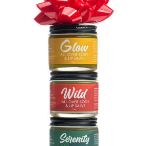 Three stacked small jars of skin care in yellow. red, and green with red ribbon.