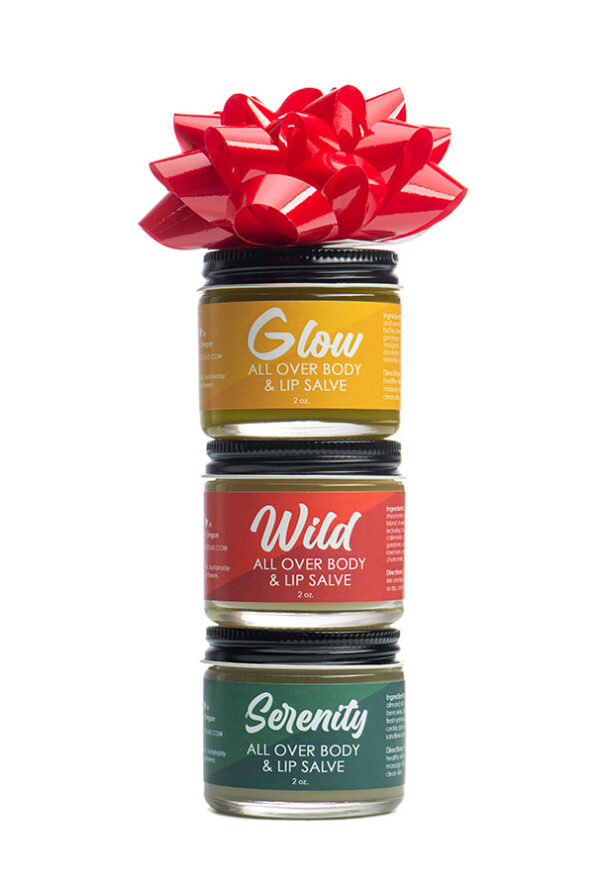 Three stacked small jars of skin care in yellow. red, and green with red ribbon.
