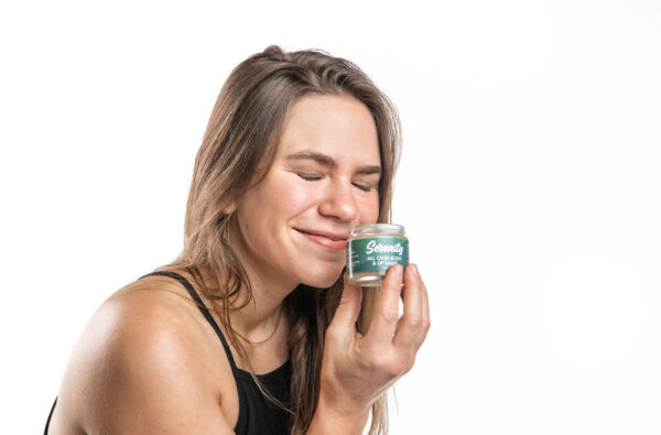 Headshot of young woman smiling while enjoying the scent of Serenity all over body and lip salve.