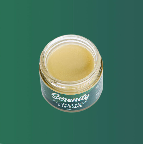 Open jar of Serenity all over body and lip salve against green background.