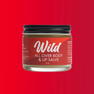 Close up jar of Wild all over body and lip salve against red background.