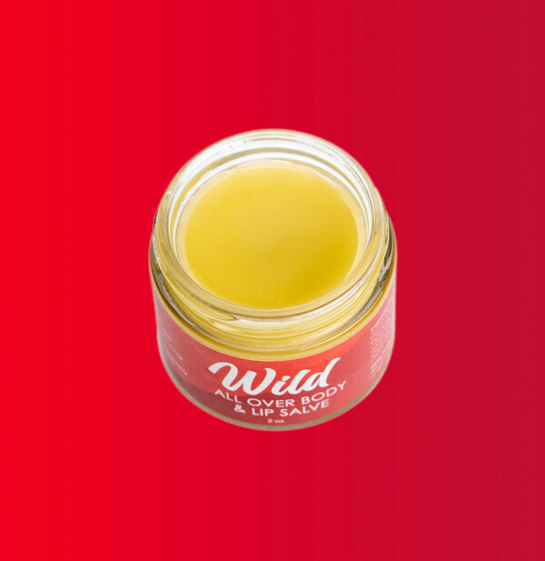 Open jar of Wild all over boy and lip salve on red background.